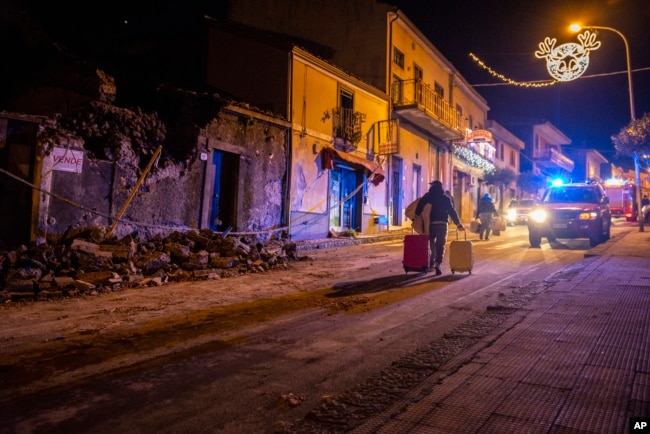 A man carries his belongings as he walks past debris of a partially collapsed house in Fleri, Sicily, Dec. 26, 2018.