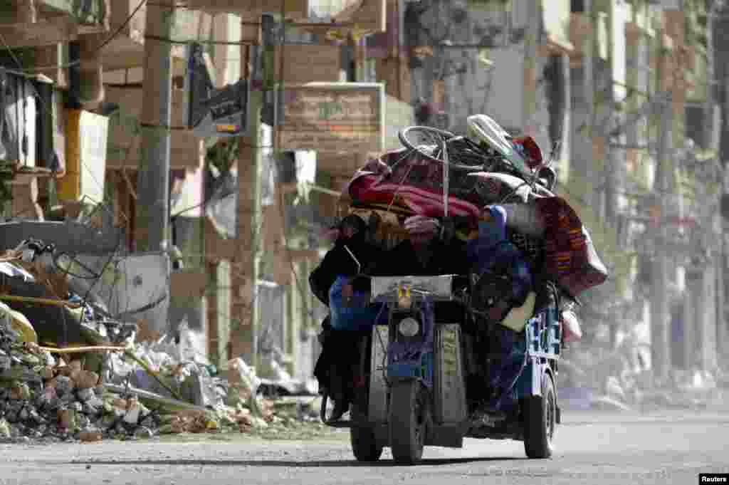 Residents ride on a motorcycle with their belongings past damaged buildings in Deir al-Zor, Syria, Oct. 9, 2013. 
