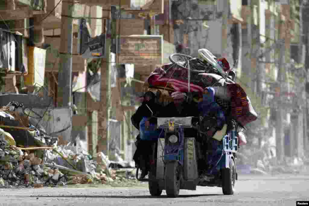 Residents ride on a motorcycle with their belongings past damaged buildings in Deir al-Zor, Syria, Oct. 9, 2013.