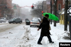 A pedestrian shelters under an umbrella as he crosses the street during a winter nor'easter snow storm in Lawrence, Massachusetts, Jan. 2, 2014.
