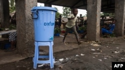 FILE - A boy runs past a dispenser containing water mixed with disinfectant, east of Mbandaka, DRC, May 23, 2018.