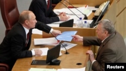 FILE- Leader of the Liberal Democratic Party Vladimir Zhirinovsky, right, passes documents to then-President-elect Vladimir Putin, Russian State Duma, Moscow, April 11, 2012.