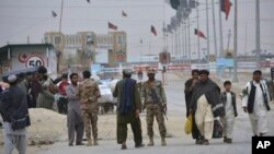 FILE - Pakistani paramilitary soldiers stand guard while people wait for the opening of a border crossing, in Chaman, Pakistan, March 20, 2017. 