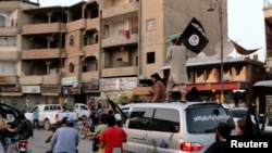 FILE - Members loyal to the Islamic State in Iraq and the Levant wave flags as they drive around Raqqa, June 29, 2014.