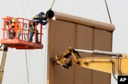 FILE - Crews work on a border wall prototype near the border with Tijuana, Mexico, Oct. 19, 2017, in San Diego, Califiornia.