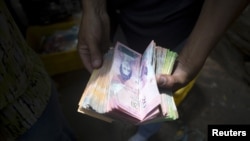 FILE - A man displays bolivar notes that he carries to pay for goods at a street market in Caracas, Venezuela, Oct. 1, 2015. 