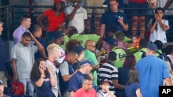Fans look on as emergency medical personnel work on a fan who fell from an upper deck at Turner Field during a baseball game between New York Yankees and Atlanta Braves, Aug. 29, 2015, in Atlanta.