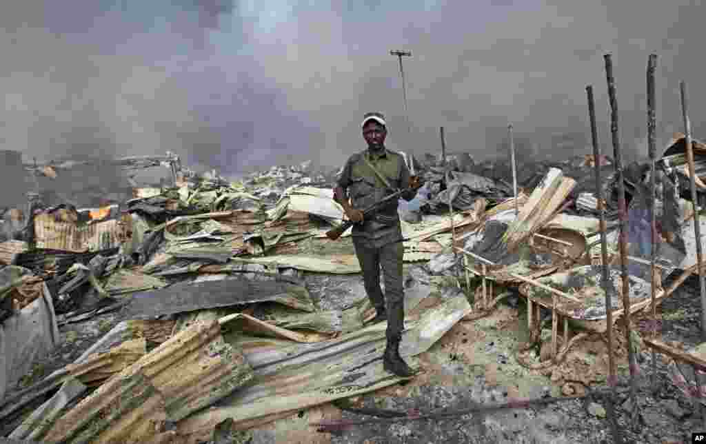 A Somali soldier walks through the wreckage after a fire engulfed the capital&#39;s main market in Mogadishu. A police officer said the overnight inferno was moved by winds which started at the gold bazaar and rapidly spread into different areas of the market, razing large buildings, shops and food stores.