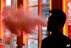 In this Feb. 20, 2014 file photo, a customer exhales vapor from an e-cigarette at a store in New York.