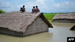 Indian children sit on the roof of a home submerged in flood waters in Batahidia on the Brahmaputra River in South Kamrup, southwest of Guwahati, July 27, 2016. 