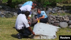 French gendarmes and police inspect a large piece of plane debris which was found on the beach in Saint-Andre, on the French Indian Ocean island of La Reunion, July 29, 2015.