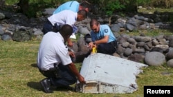 French gendarmes and police inspect a large piece of plane debris that was found on the beach in Saint-Andre, on Reunion Island in the Indian Ocean, July 29, 2015.