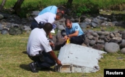 FILE - French gendarmes and police inspect a large piece of plane debris which was found on the beach in Saint-Andre, on the French Indian Ocean island of La Reunion, July 29, 2015.