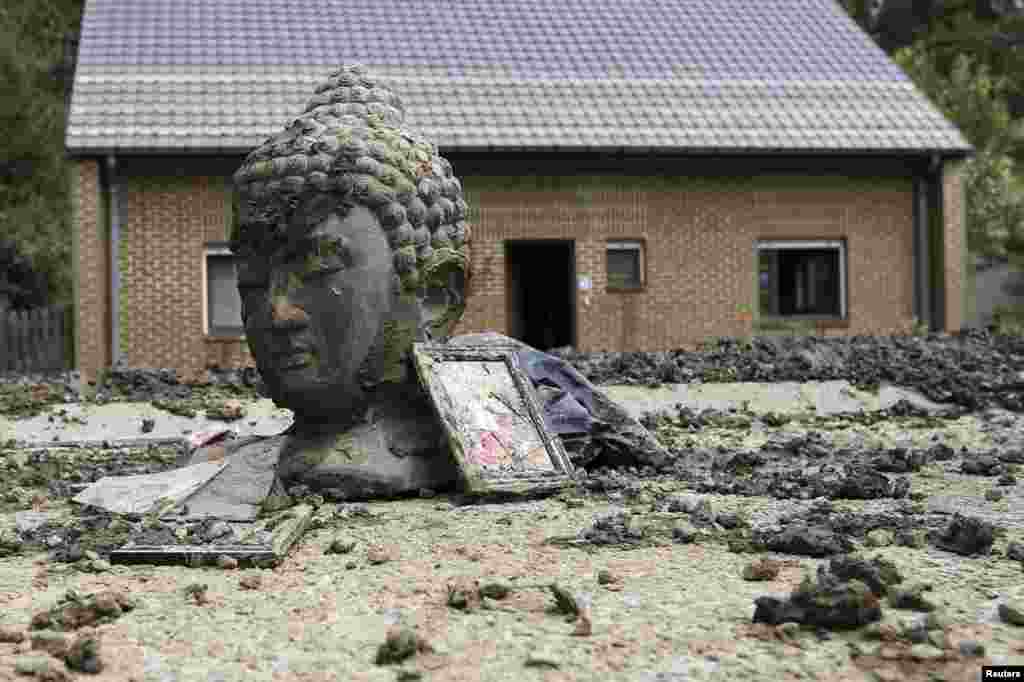 Một bức tượng Phật và những mảnh vỡ bị bùn bao phủ bên ngoài một ngôi nhà bị ngập lụt sau khi mưa lớn do bão ập xuống thị trấn Ittre, Bỉ. 