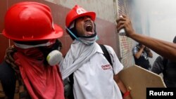 Manifestantes opositores tratan de limpiar de gas lacrimógeno a un compañero durante choques con la policía en Caracas el 3 de mayo.