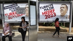 Commuters wait at a bus stop as posters of Turkish Prime Minister Recep Tayyip Erdogan are sen in the background in Istanbul, Turkey, June 10, 2011