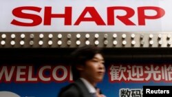 Seorang turis China berjalan melewati logo Sharp terlihat di luar toko retail elektronik di Tokyo, Jepang, 30 Maret 2016.