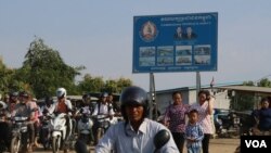 Commuters are about to take a ferry from Kandal province to Phnom Penh. Behind them is the Cambodian People’s Party’s sign bearing the party logo and the faces of Prime Minister Hun Sen and National Assembly President Heng Samrin, Jan. 10, 2018. (Sun Narin/VOA Khmer)