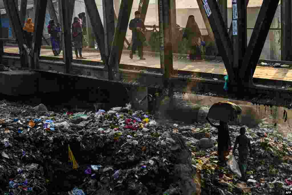 A Bangladeshi woman (lower R) carries recyclable waste over piles of trash underneath a pedestrian bridge in Dhaka, Bangladesh.