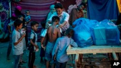 A Rohingya activist distributes new clothes among refugees at a refugee camp alongside the banks of the Yamuna River in the southeastern borders of New Delhi, sprawling Indian capital, July 1, 2021. (AP Photo/Altaf Qadri)