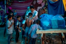 Seorang aktivis Rohingya membagikan pakaian baru kepada para pengungsi di sebuah kamp pengungsi di sepanjang tepi Sungai Yamuna di perbatasan tenggara New Delhi, 1 Juli 2021. (Foto: AP/Altaf Qadri)