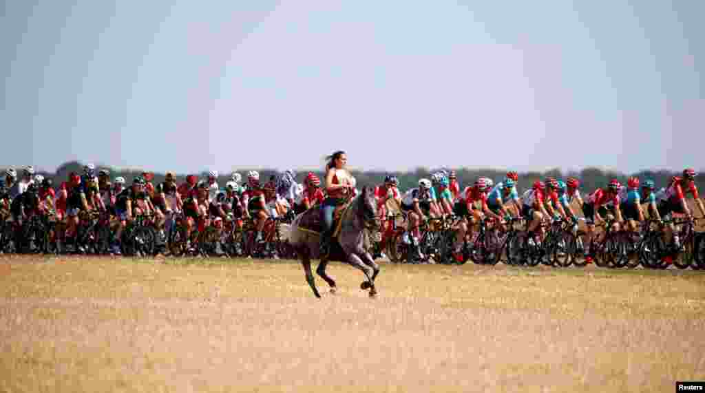 A woman rides a horse as the pack of riders passes during the 216-km Stage 6 tour de Fracne cycling race from Vesoul to Troyes, France.