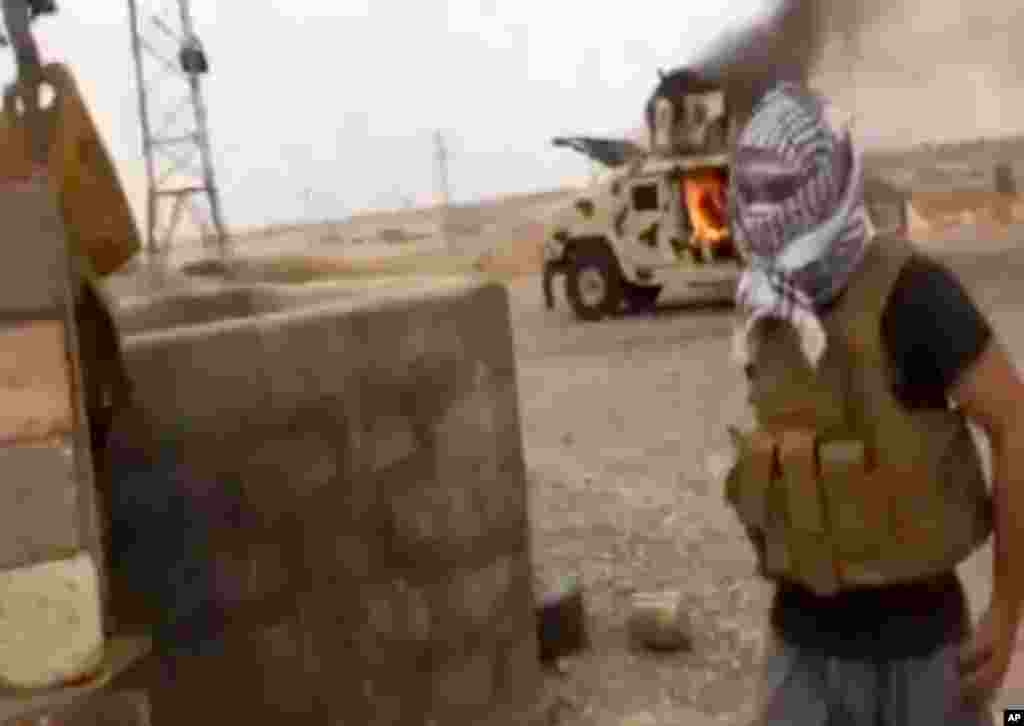 This image from video posted by Iraqi0Revolution, a group supporting ISIL, shows a militant standing in front of a burning Iraqi Army Humvee in Tikrit, Iraq, June 11, 2014.