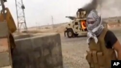 This image from video posted by Iraqi Revolution, a group supporting ISIL, shows a militant standing in front of a burning Iraqi Army Humvee in Tikrit, Iraq, June 11, 2014.