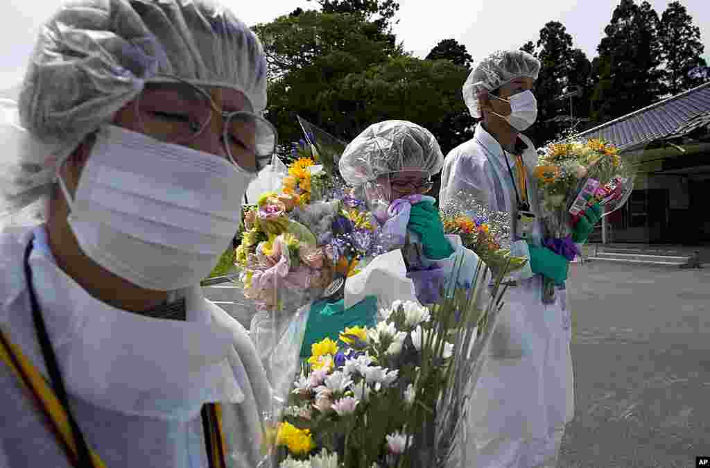 Mourners in protective suits hold flowers at a memorial ceremony for residents from the town of Okuma, inside the contaminated exclusion zone near the crippled Fukushima Dai-Ichi nuclear power plant, July 24, 2011. (AP)