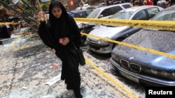 A woman walks over shattered glass, past damaged cars near the site of an explosion in Beirut's southern suburbs, Jul. 9, 2013.