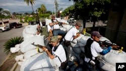 FILE - In this Jan. 12, 2014 file photo, men belonging to the Self-Defense Council of Michoacan, ride on a sandbag-filled truck while trying to flush out alleged members of The Caballeros Templarios drug cartel from the town of Nueva Italia, Mexico.