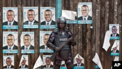 A Ugandan riot policeman blocks the gate of the party headquarters of opposition leader Kizza Besigye, shortly after raiding the premises for the second time in a week, in the capital Kampala, Uganda, Feb. 22, 2016. 
