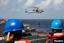 Sailors aboard the amphibious assault ship USS Kearsarge (LHD 3) observe as an MH-60 Sea Hawk helicopter transfers pallets of supplies from the fast combat support ship USNS Supply (T-AOE 6) during replenishment-at-sea for continuing operations.