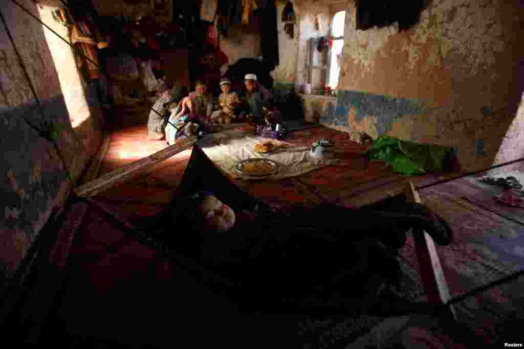 An ethnic Hazara child sleeps as the rest of the family eat a meal in their home in Turkman camp in Nowshera, Pakistan.