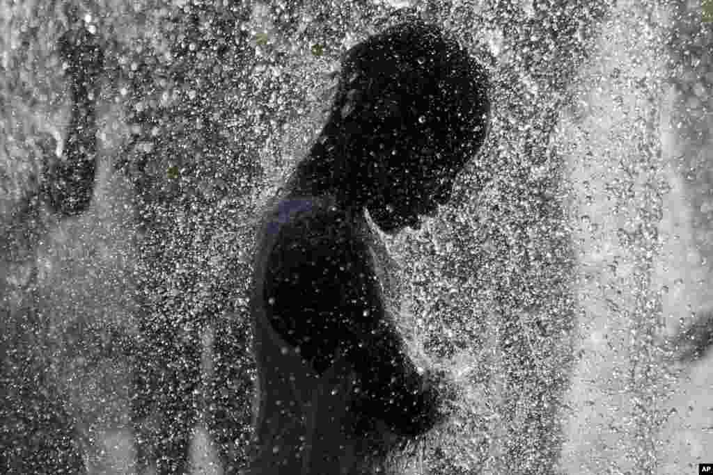 خنک شدن پسر بچه در زیر فواره آب سرد در پارکی در تل آویو