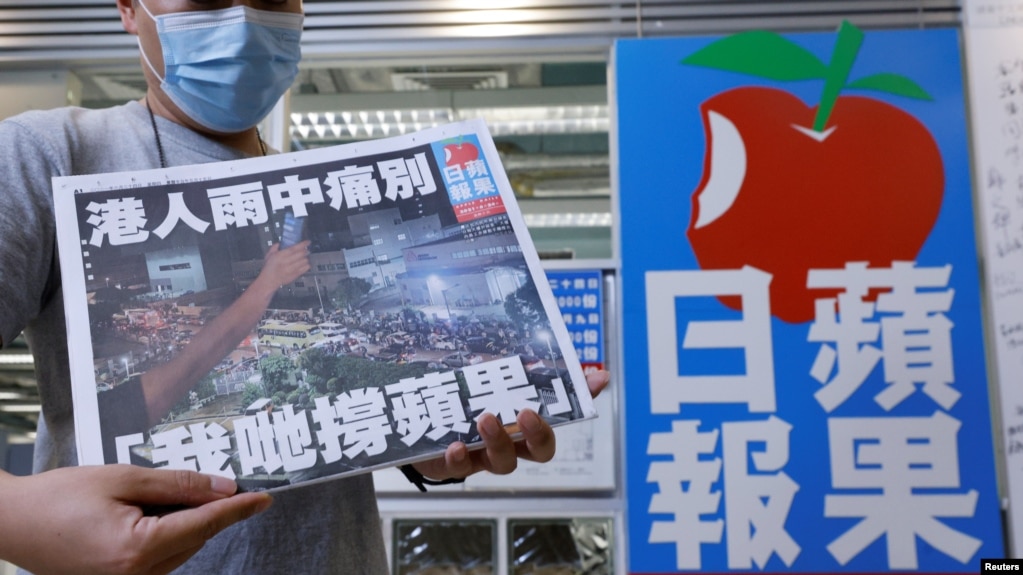 资料照：一名香港苹果日报员工在总部大楼的标识前手举最后一日发行的苹果日报。（2021年6月24日）(photo:VOA)