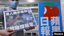 资料照：一名香港苹果日报员工在总部大楼的标识前手举最后一日发行的苹果日报。（2021年6月24日）