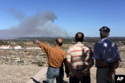 Men in Abrantes, central Portugal, watch a forest fire burning on the hills outside the city, Aug.11, 2017.