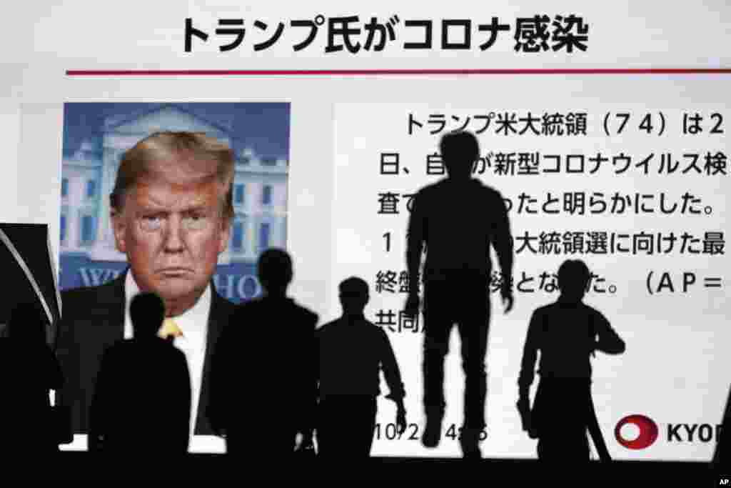 People walk past a screen showing the news report that President Donald Trump has tested positive for the coronavirus, Friday, Oct. 2, 2020, in Tokyo