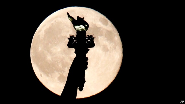 In this July 31, 2015, file photo, a full moon rises behind the torch of the Statue of Liberty as seen from Liberty State Park in Jersey City, N.J. But what does it mean "to carry a torch for someone"? Read on to find out! (AP Photo/Julio Cortez)