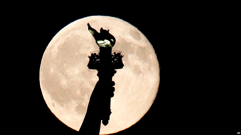 In this July 31, 2015, file photo, a blue moon rises behind the torch of the Statue of Liberty seen from Liberty State Park in Jersey City, N.J. A blue moon happens when the moon rises in its full stage twice during the same month. (AP Photo/Julio Cortez)