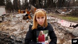 Christina Taft, the daughter of Camp Fire victim Victoria Taft, poses with a photo of her mother, at the burned out ruins of the Paradise, California, home where she died last fall, Feb. 7, 2019. 