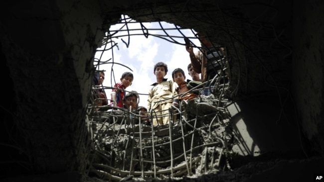 FILE - Boys look through a hole made by a Saudi-led airstrike on a bridge in Sana'a, Yemen, March 23, 2016.