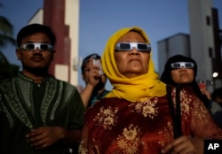 People look up at the sun wearing protective glasses to watch a solar eclipse in Jakarta, Indonesia, Wednesday, March 9, 2016.
