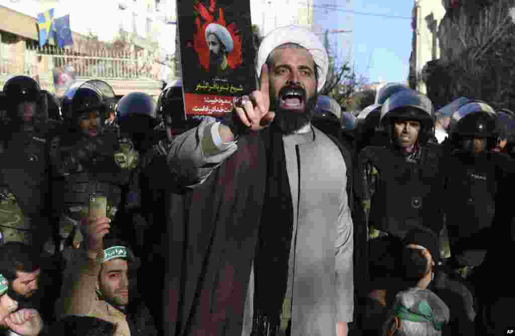 Surrounded by policemen, a Muslim cleric addresses a crowd during a demonstration to protest the execution of Saudi Shiite Sheikh Nimr al-Nimr, shown in the poster in background, in front of the Saudi embassy in Tehran, Iran, Sunday, Jan. 3, 2016.