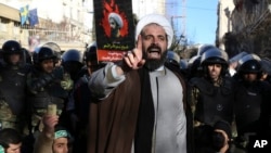 Surrounded by policemen, a Muslim cleric addresses a crowd during a demonstration to protest the execution of Saudi Shiite Sheikh Nimr al-Nimr, shown in the poster in background, in front of the Saudi embassy in Tehran, Iran, Sunday, Jan. 3, 2016.