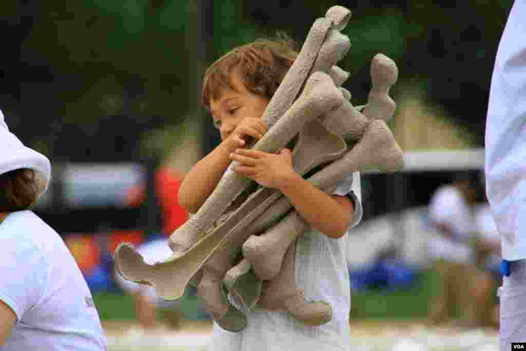 Child volunteer carries symbolic bones for display at the "One Million Bones" installation on the National Mall, Washington, D.C, June 8, 2013. (Jill Craig/VOA)