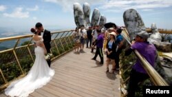 A couple stand near giant hands structure for their wedding photos on Gold Bridge on Ba Na hill near Danang city, Vietnam August 1, 2018. REUTERS/Kham - RC1F1CE07A50