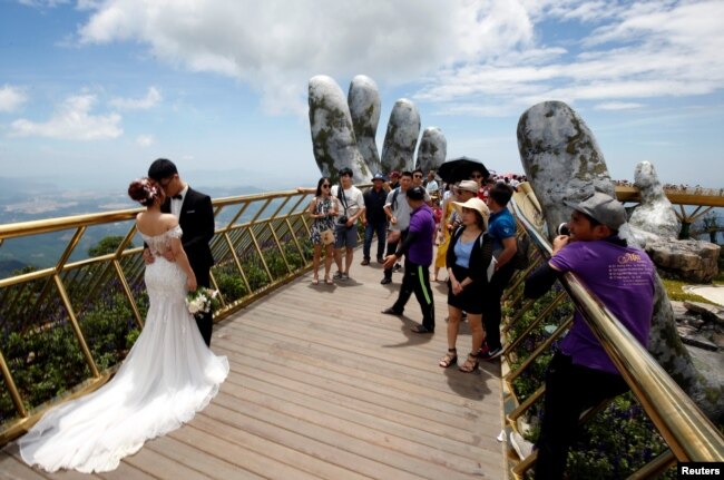 A couple stand near giant hands structure for their wedding photos on Gold Bridge on Ba Na hill near Danang city, Vietnam August 1, 2018. REUTERS/Kham