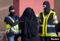 FILE - Masked Spanish police officers lead a detained woman in Melilla in December 2014, in a crackdown on efforts to recruit women to go to Syria and Iraq to support the Islamic State.
